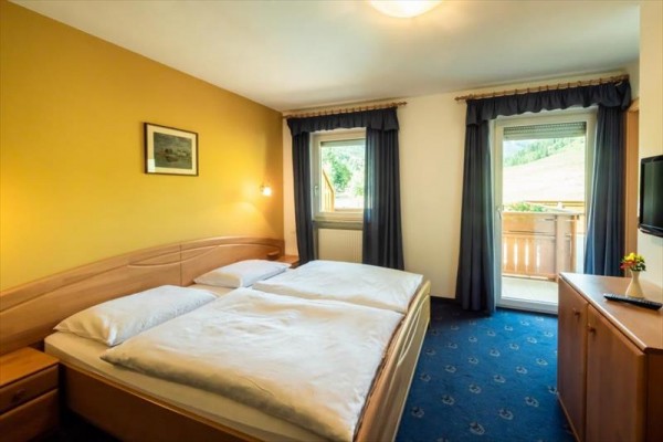 Izba s veľkou posteľou, žltou stenou a balkónom s výhľadom do prírody.