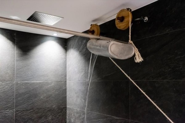 Zavesené kovové zariadenie s dvoma kladkami a lanom nad dlaždicami v kúpeľni.  