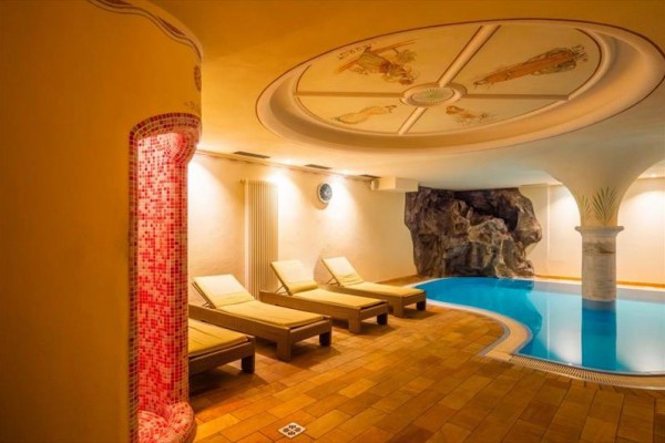 Oddychová zóna s ležadlami a bazénom v interiéri s dekoratívnym stropom.