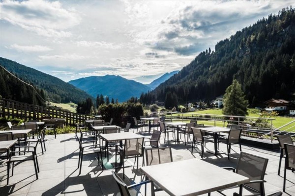 Horská terasa s prázdnymi stolmi a stoličkami s výhľadom na lesy a údolie.