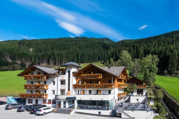 Hotel obklopený zelenými lúkami a lesmi počas slnečného dňa.