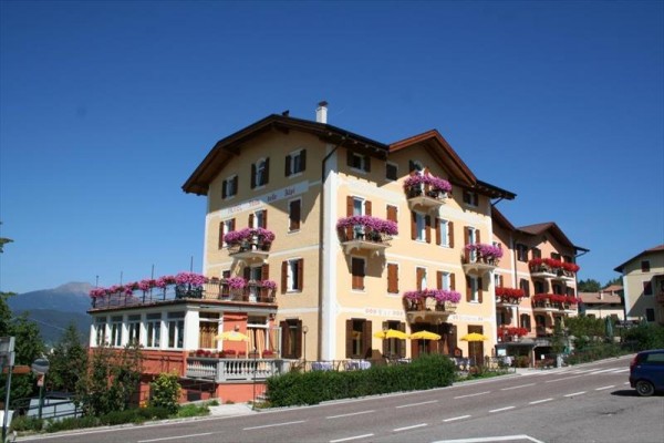 Trojposchodový hotel s balkónmi ozdobenými kvetmi pri ceste za slnečného dňa.