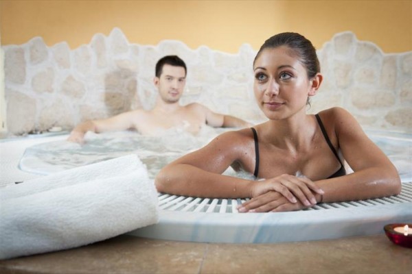 Dvaja ľudia relaxujú vo vírivke obklopení kamennou stenou.