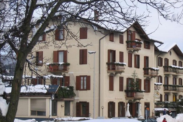 Zasnežený hotel s hnedými okenicami a balkónmi, pred ktorým stojí strom.