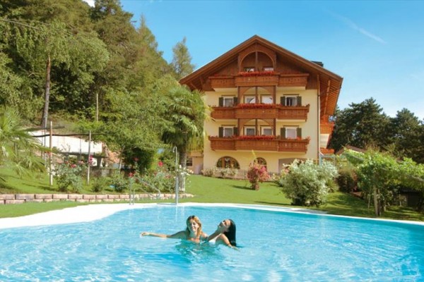 Dve ženy si užívajú bazén pred malebným horským hotelom.