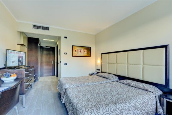 Dve samostatné postele v svetlej hotelovej izbe s moderným nábytkom.  