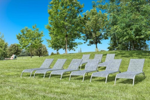 Osem lehátok na trávniku s pozadím stromov a jasnej oblohy.