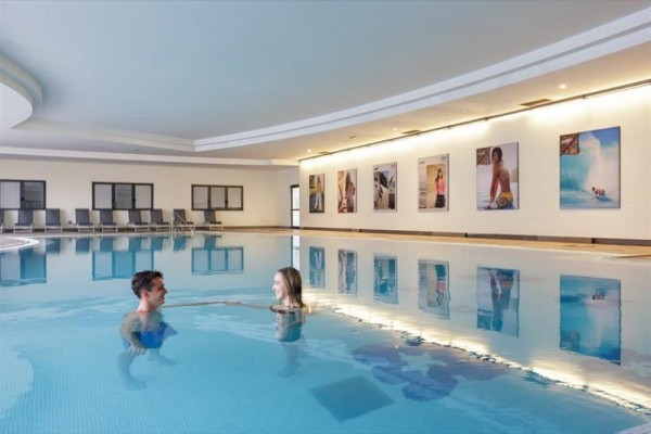 Dvaja ľudia v krytom bazéne neďaleko steny s fotografiami.  