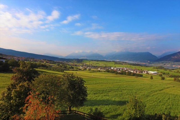 Rozľahlá krajina s lúkami, stromami a horami v pozadí.