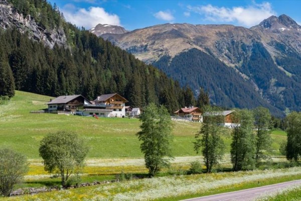 Malebná horská krajina s lesmi, lúkami a domami na úpätí kopcov.
