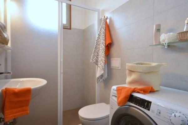 Kúpeľňa s práčkou, umývadlom, toaletou a sprchovacím kútom, ozdobená oranžovými doplnkami.