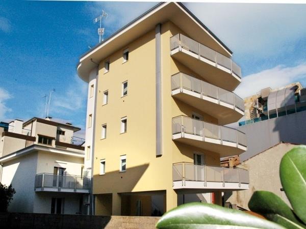 Svetlá štvrtposchodová budova s balkónmi a anténou na streche.