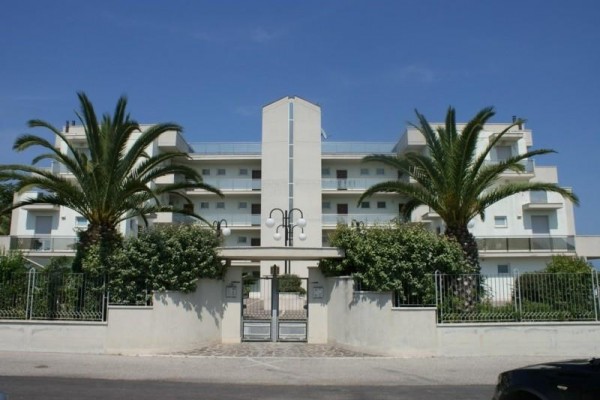 Moderná viacposchodová budova s dvoma palmami pri vchode.