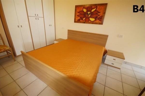 Spálňa s dvojlôžkom, oranžovým prehozom a obrazom slnka nad posteľou.