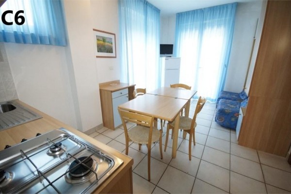 Kuchyň s jedálenským stolom a stoličkami, vedľa ktorej je pohovka a okno s modrými závesmi.