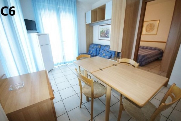 Pohľad do svetlej miestnosti s jedálenským stolom, stoličkami, pohovkou a chladničkou.