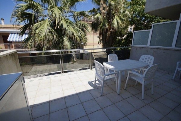 Slnečná terasa s bielym plastovým nábytkom a palmami v pozadí.