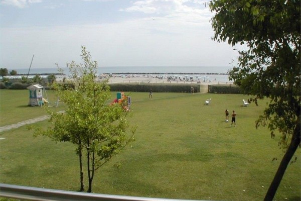 Pobrežná pláž s ľuďmi a zeleným trávnikom v popredí.