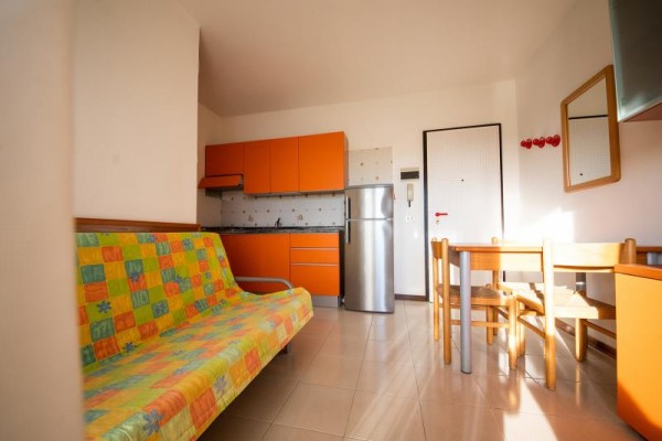 Moderná kuchyňa s oranžovými skrinkami a pohovkou so farebným prehozom.