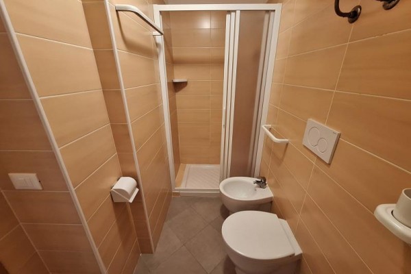 Kúpeľňa s oranžovými kachličkami, sprchovacím kútom, WC a bidetom.