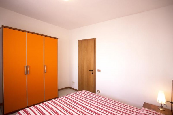 Spálňa s oranžovou skriňou, drevenými dverami a posteľou s pruhovanou bielizňou.