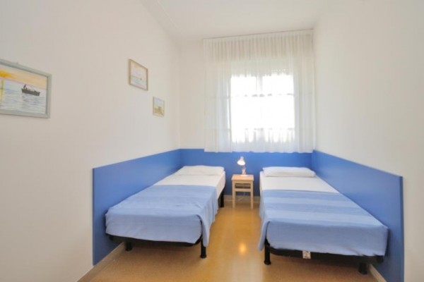 Dve jednolôžka s modrými prikrývkami oddelené malým stolíkom, uprostred miestnosti s bielymi stenami.
