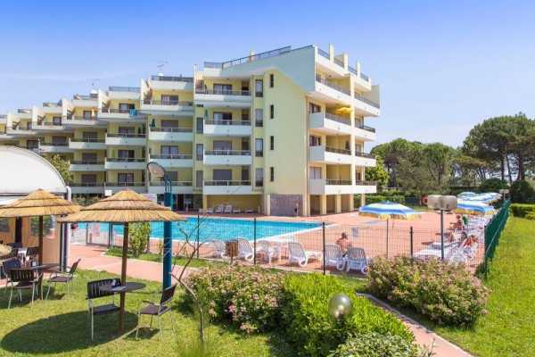 Budova s apartmánmi pri vonkajšom bazéne obklopenom ležadlami a slnečníkmi.