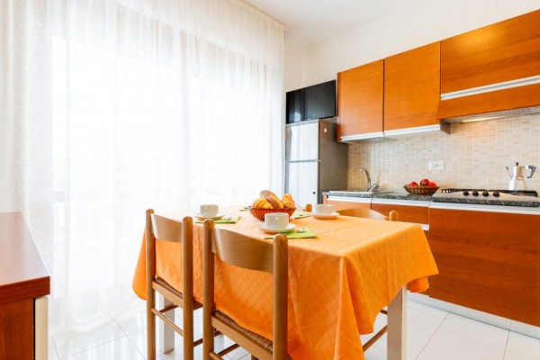 Svetlá kuchyňa s dreveným nábytkom a prestretým stolom s oranžovým obrusom.