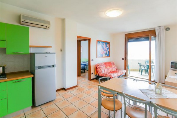 Moderná obývačka s kuchyňou v zelených farbách, pohovkou a prístupom na balkón.  