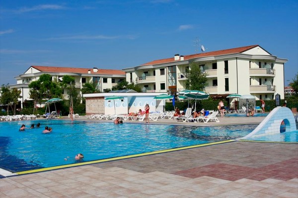 Vonkajší bazén s ľuďmi pri niekoľkých bielych budovách a slnečníkmi okolo.