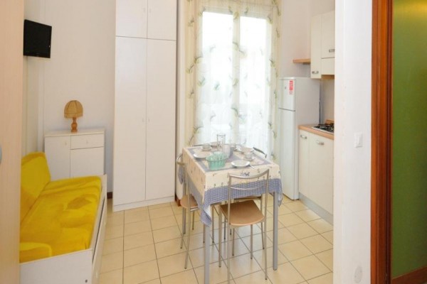 Malá kuchyňka s jedálenským stolom, stoličkami a žltou sedačkou v svetlo zariadenom priestore.