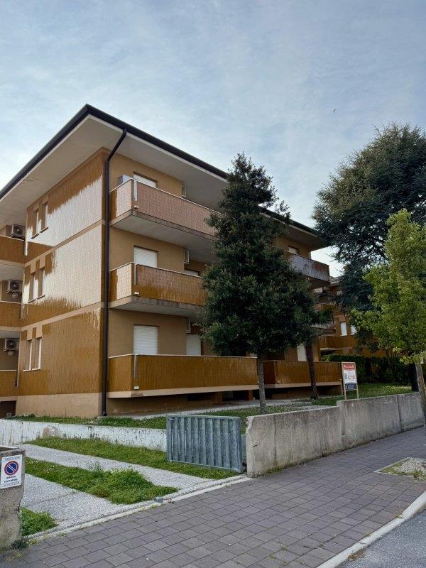 Trojposchodový bytový dom s balkónmi obklopený stromami.