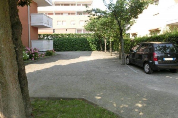 Parkovacie miesto vedľa čierneho auta pri vedľajších budovách a živom plote.  