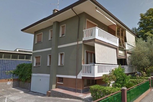 Dvojpodlažný dom s balkónom a zeleňou okolo.