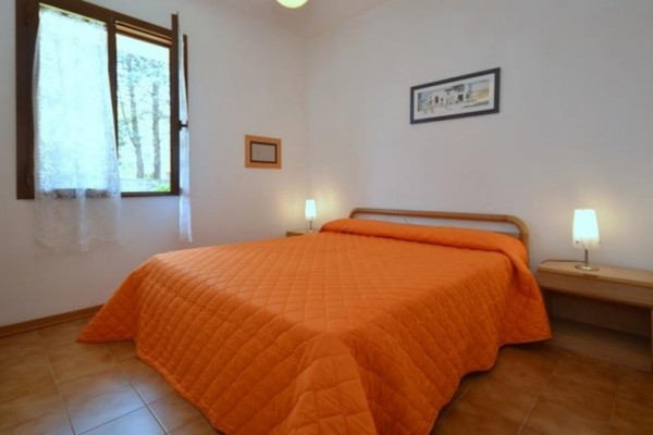 Spálňa s oranžovým prehozom na posteli, nočnými stolíkmi a otvoreným oknom.