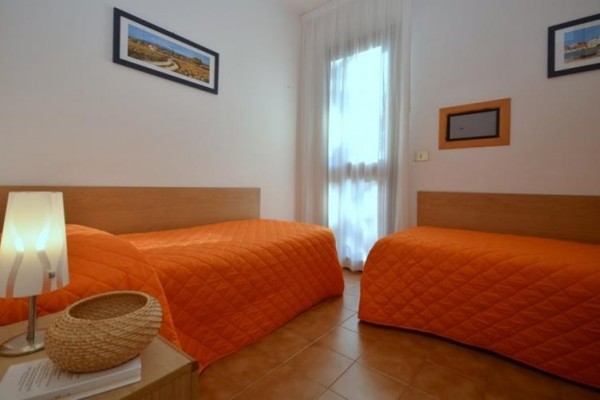 Dve jednolôžkové postele s oranžovými prikrývkami a lampou na nočnom stolíku.