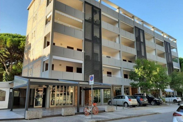 Moderná päťposchodová budova s balkónmi a zaparkovanými autami pred ňou.