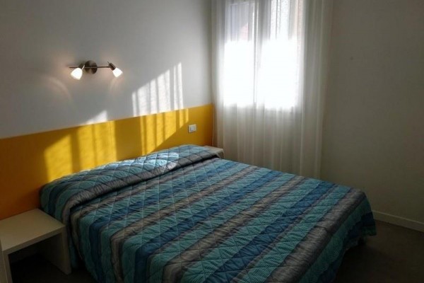 Presvetlená spálňa s dvojlôžkom, žltým čelom a pruhovaným prehozom.