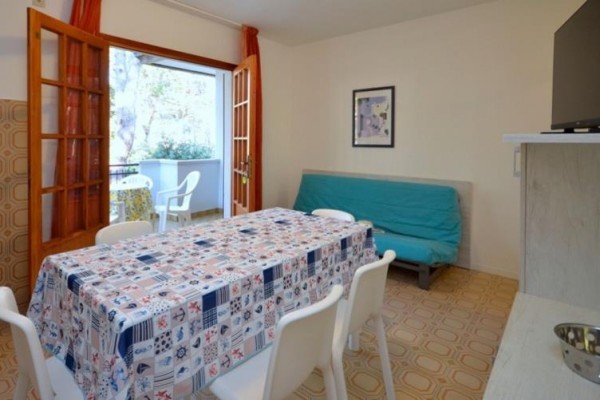 Obytná miestnosť s jedálenským stolom, stoličkami, rozkladacou pohovkou a otvorenými dverami na balkón.