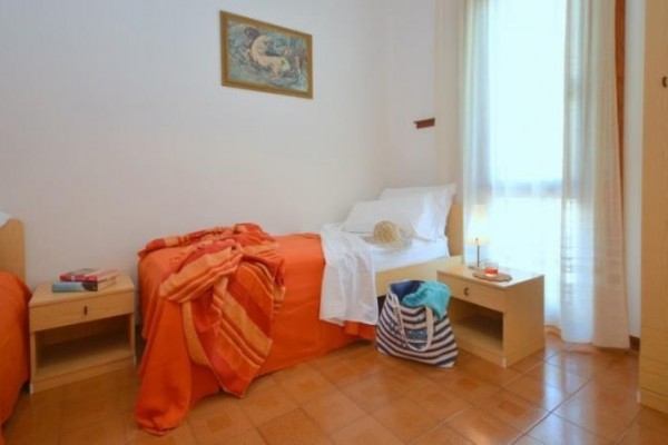 Dve jednolôžkové postele s oranžovými obliečkami, nočné stolíky a závesy, na jednom stole klobúk a taška.
