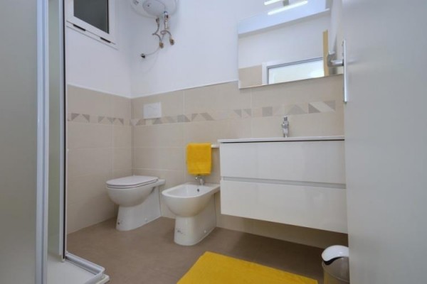 Moderná kúpeľňa s bidetom, toaletou a umývadlom, doplnená žltými doplnkami.