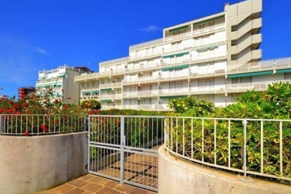 Bytový dom s bielymi balkónmi obklopený zeleňou pod modrou oblohou.