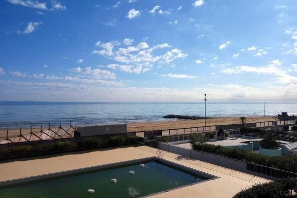 Pohľad na bazén, pláž a kľudné more za slnečného dňa.