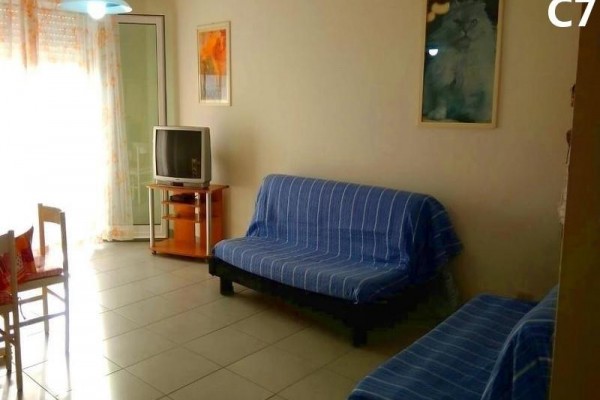 Obývačka s modrým gaučom, starším televízorom a obrazmi na stenách.