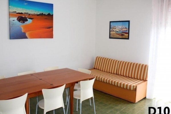 Jedáleň s dreveným stolom, bielymi stoličkami, oranžovou pohovkou a dvoma obrazmi na stene.