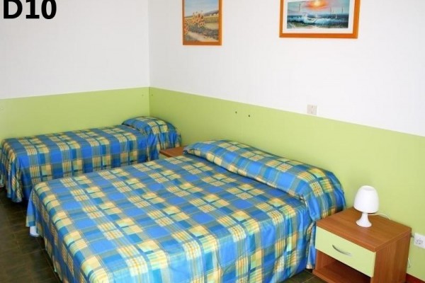 Dve jednolôžkové postele s modro-žltými kockovanými prikrývkami a nočným stolíkom s lampou v miestnosti.