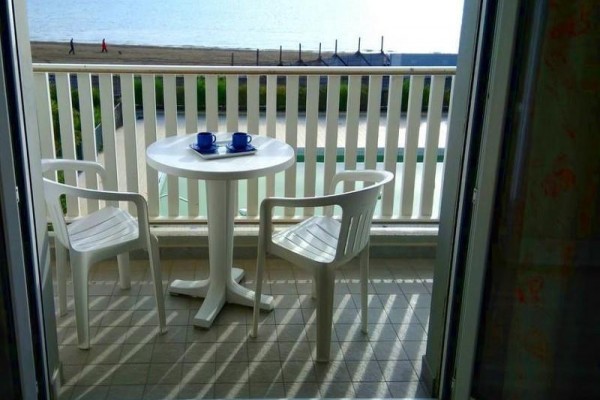 Balkón s plastovým stolíkom, dvoma stoličkami a výhľadom na more.