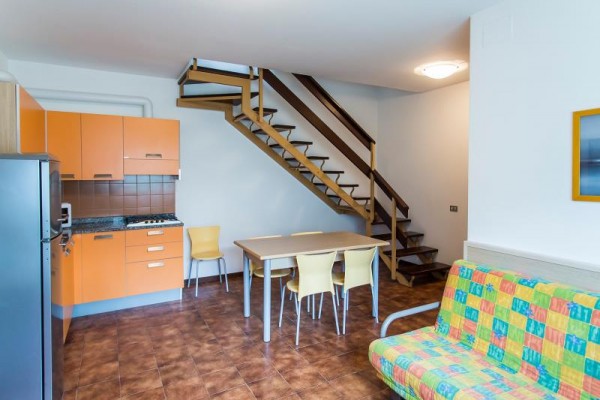 Moderný interiér s kuchynským kútom, jedálenským stolom a schodiskom.