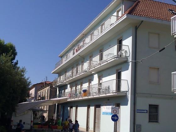 Biela trojposchodová budova s balkónmi v meste za slnečného počasia.