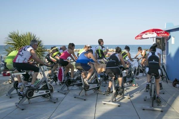 Skupina ľudí cvičí na stacionárnych bicykloch vonku pri mori.